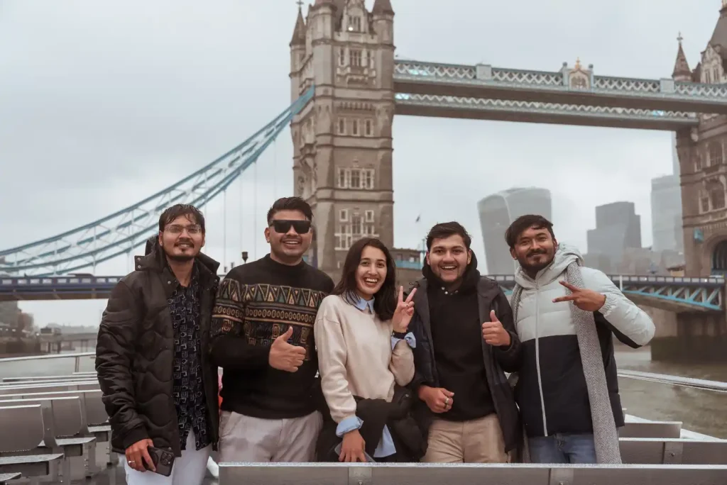 A group of friends enjoying a boat ride on the River Thames, with the Tower Bridge in the background. 