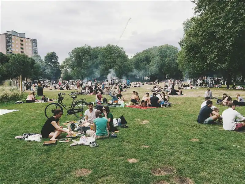 A diverse group of people enjoying a picnic in a London park. 
